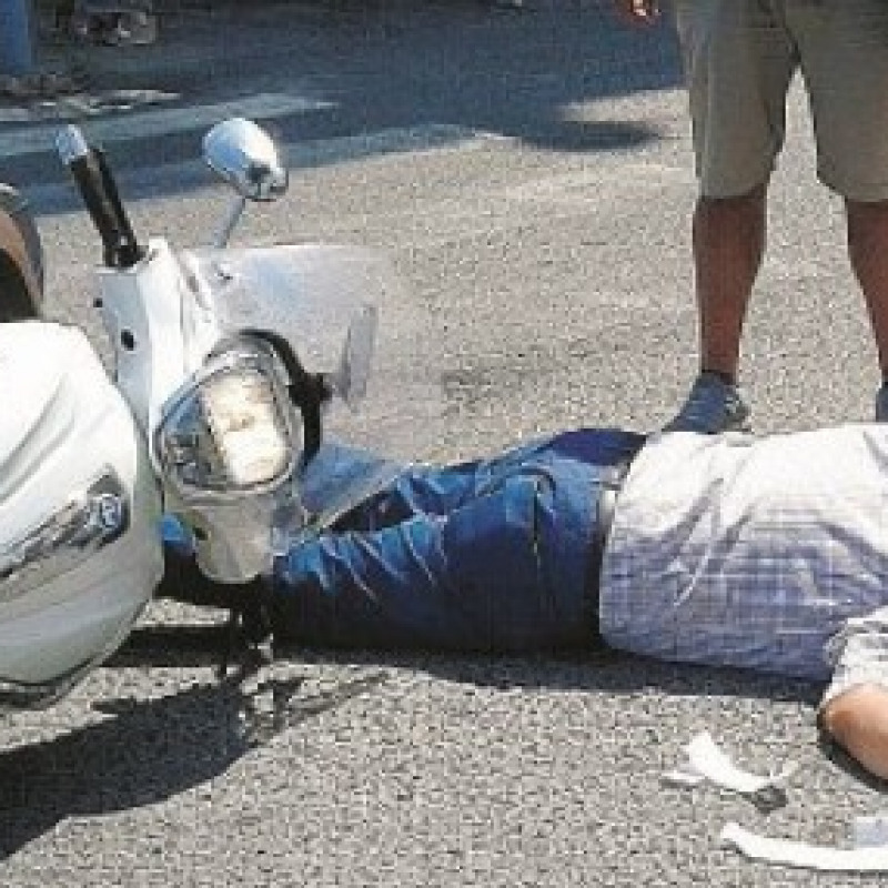 Motociclista sull'asfalto dopo schianto con auto