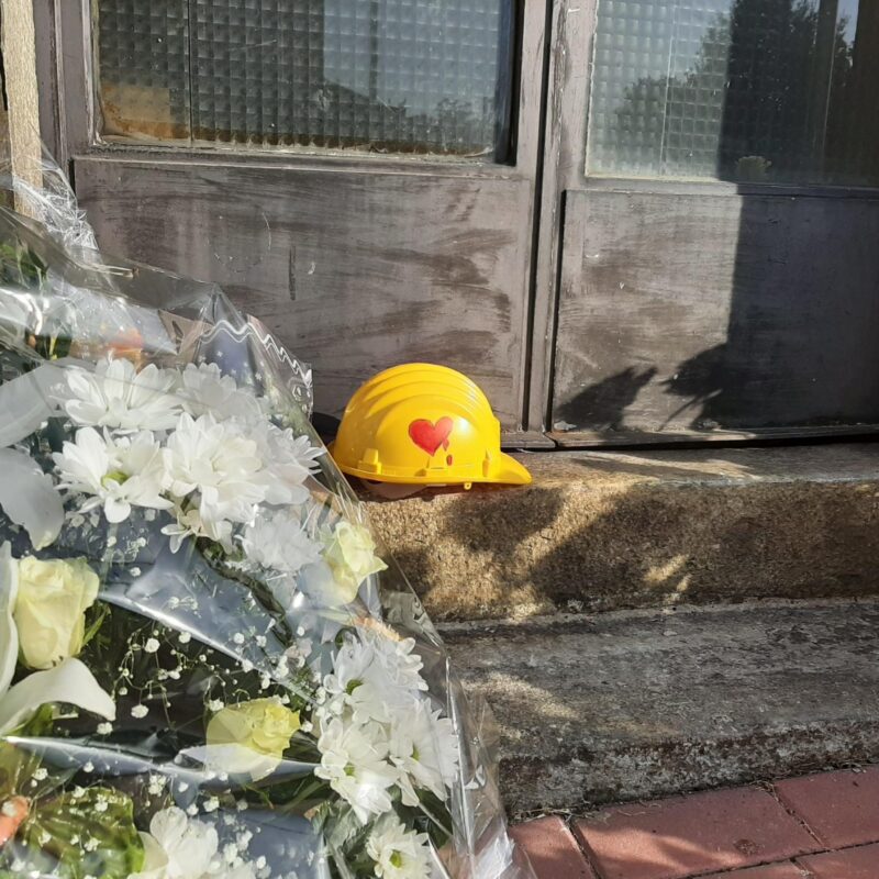Mazzi di fori e un casco di protezione giallo, con disegnato su un lato un cuore rosso che sanguina, su di uno scalino di una porta d'ingresso della stazione di Brandizzo, dove cinque operai sono morti travolti da un treno