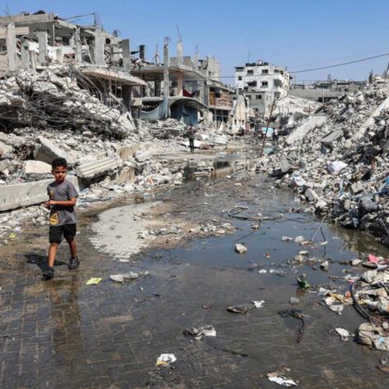 A boy walks through a puddle of sewage water past mounds of trash and rubble along a street in the Jabalia camp for Palestinian refugees in the northern Gaza Strip on August 14, 2024 amid the ongoing conflict in the Palestinian territory between Israel and Hamas. (Photo by Omar AL-QATTAA / AFP)