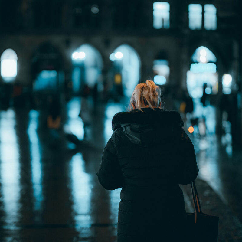 A blonde woman in a coat standing in the street at night