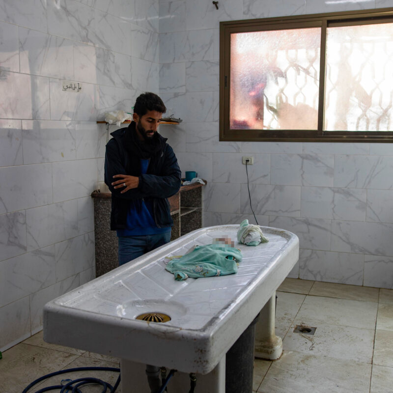 epa11793926 The body of three-week-old girl Sila lies on an autopsy table as her father (L) looks on, in the morgue of the Nasser Hospital in Khan Younis, southern Gaza Strip, 25 December 2024 (issued 26 December 2024). According to forensic doctors at the hospital, the baby died of exposure to extreme cold inside her tent in Mawasi.