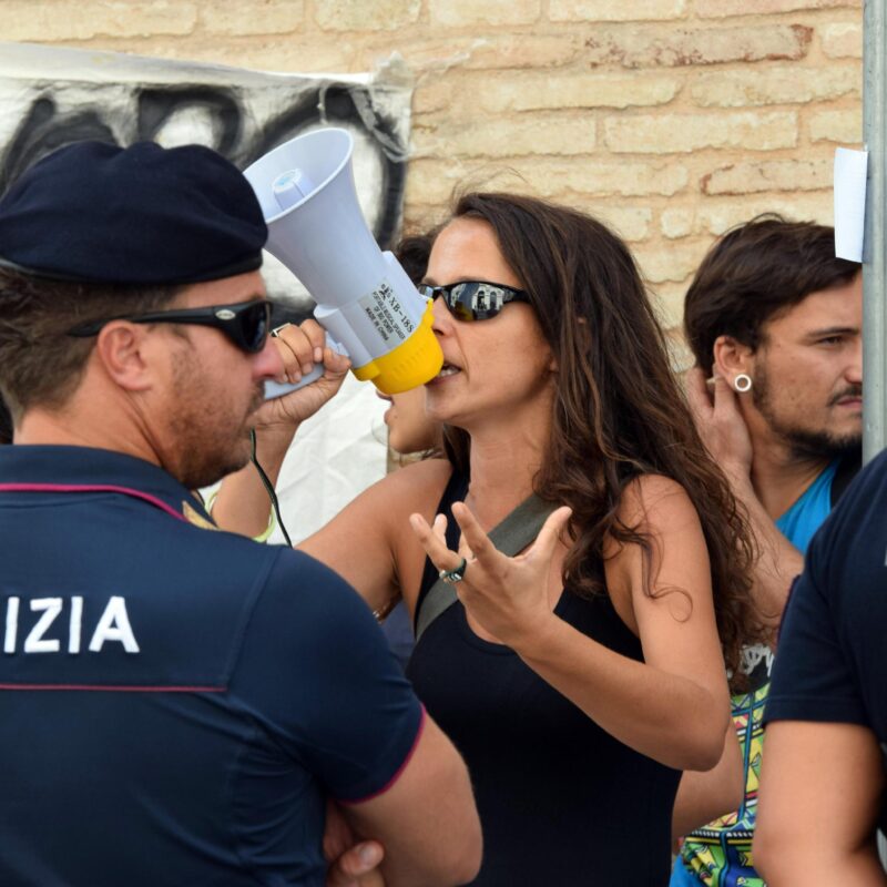 Canotta nera, occhiali da sole scuri fascianti e tanta rabbia. Veronica Padoan, figlia del ministro dell'Economia, da qualche tempo paladina dei braccianti-schiavi del ghetto di Rignano, ha atteso pazientemente davanti alla prefettura di Foggia l'arrivo del ministro della Giustizia, Andrea Orlando, impegnato per un vertice sul caporalato. Con un megafono ha denunciato la piaga degli schivi delle campagne e, assieme ad una quindicina di migranti, ha esposto un lenzuolo con una scritta rossa e nera: "Sul nostro lavoro decidiamo noi. We need yes".ANSA/FRANCO CAUTILLO